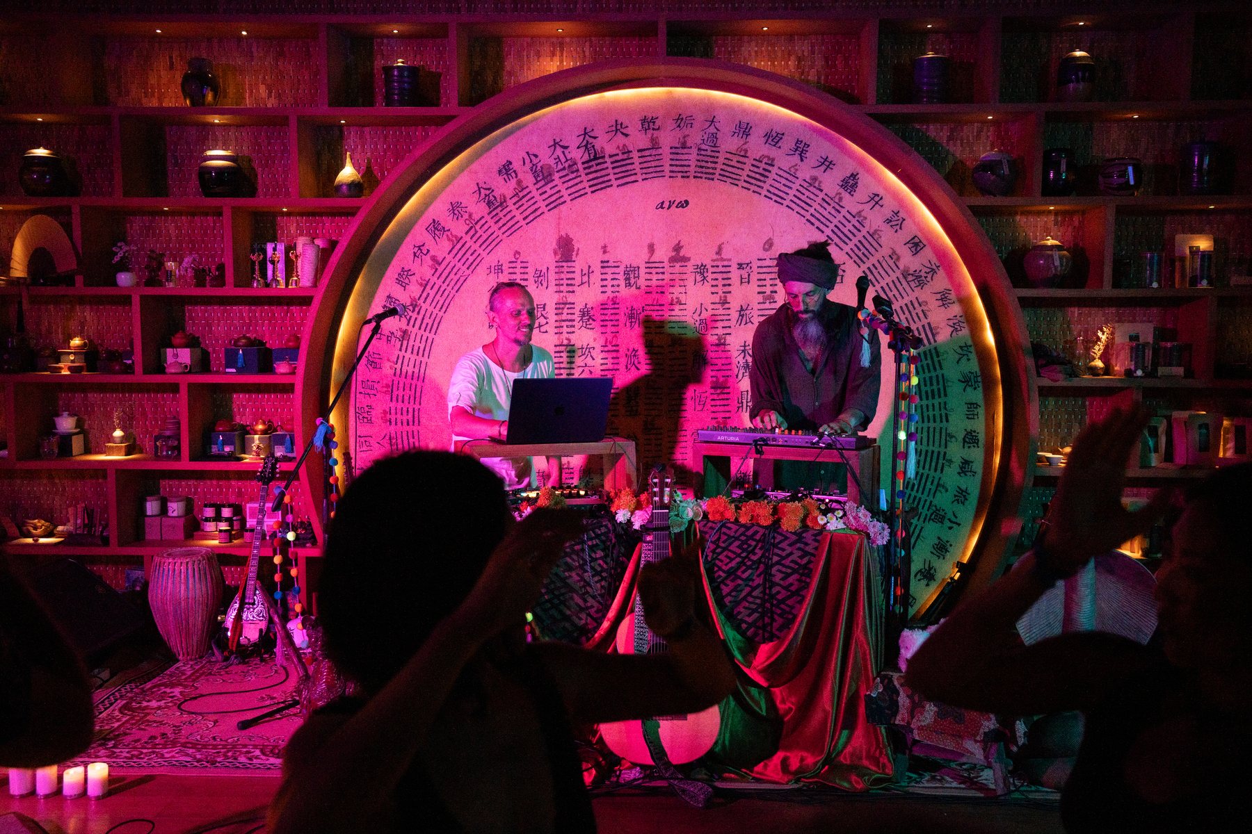 Acharya performing live with keys in front of a glowing circular stage, dancers in the foreground