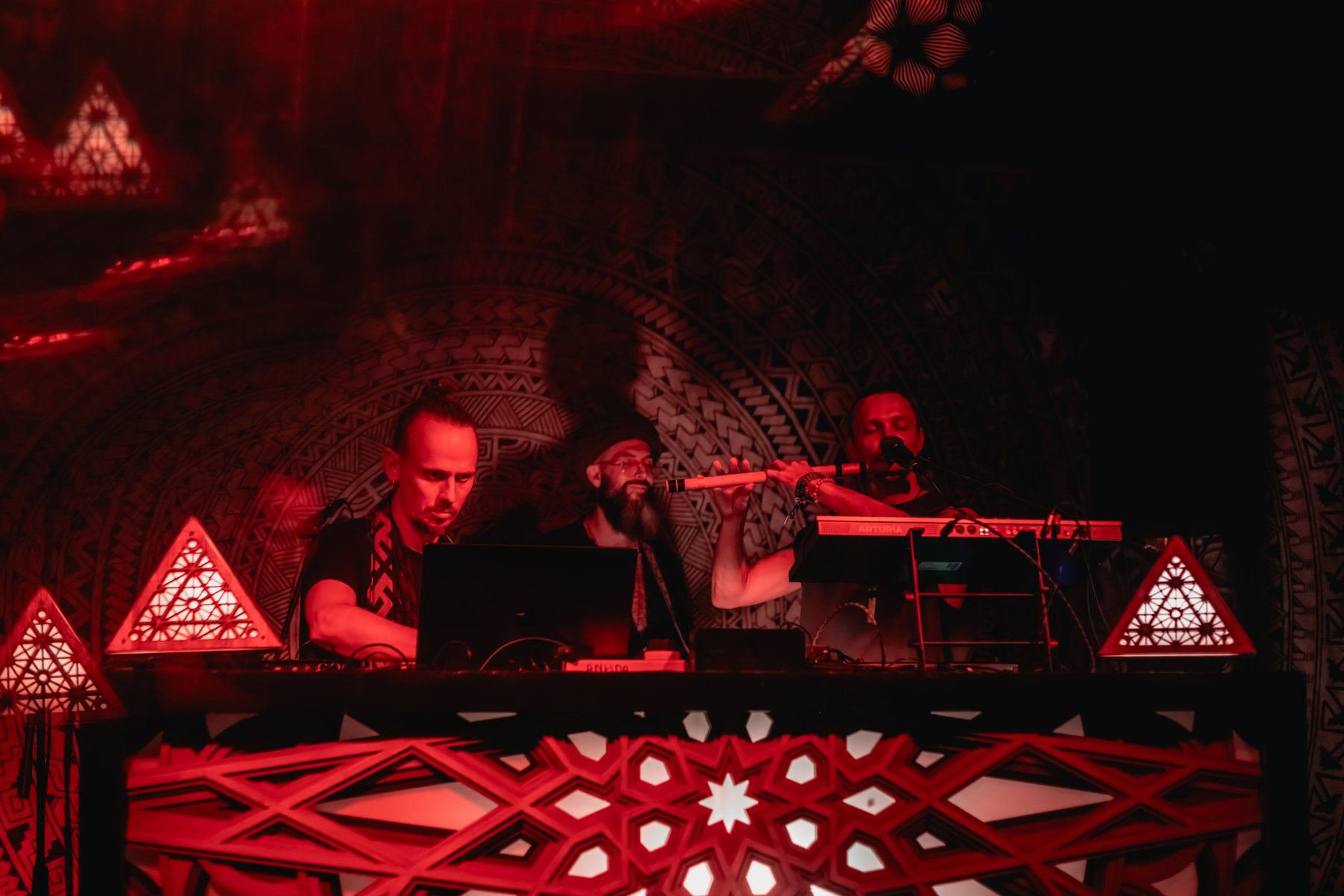 Acharya performing live with flute and keys on a red-lit stage